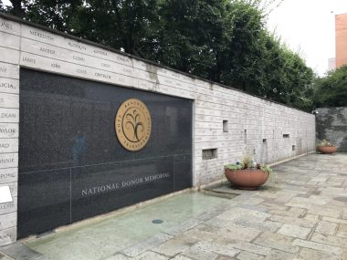 pulmonary fibrosis lung transplant | Pulmonary Fibrosis News | a photo of the courtyard of the National Donor Memorial, made of walls of gray rectangular stone with etchings on them. A black section of the wall has an emblem and the words "NATIONAL DONOR MEMORIAL" 