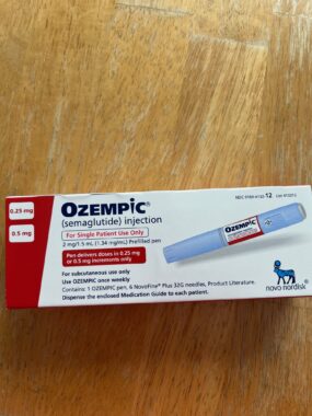 A box containing an Ozempic (semaglutide) injection lies on a brown wooden table.