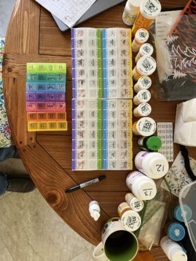 A photo taken from an aerial perspective shows a table covered with pill organizers and pill bottles.