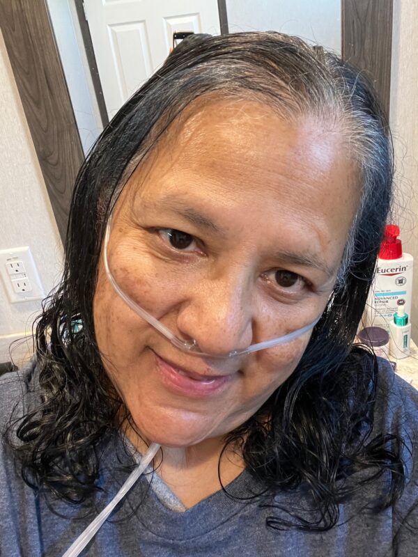 A 57-year-old woman wearing an oxygen cannula takes a close-up selfie in her home. 