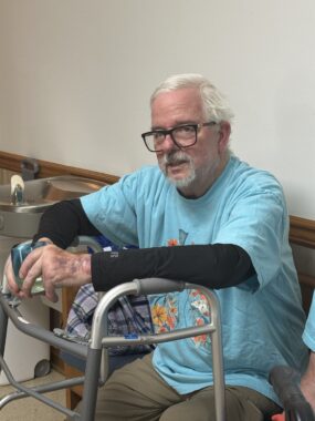 A man sits on a bench, resting against a walker.